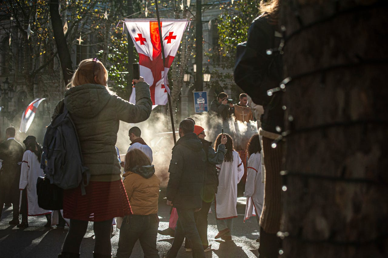 portfolio-04 A vibrant street procession in Tbilisi, Georgia, featuring Georgian flags and traditional attire.